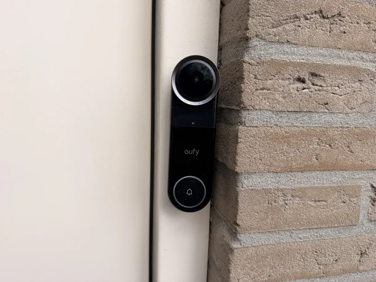 Eufy Video Doorbell S4 recht van voren op een houten kozijn naast een bakstenen muurtje