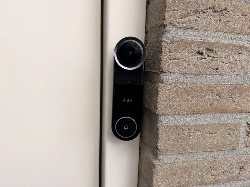 Eufy Video Doorbell S4 recht van voren op een houten kozijn naast een bakstenen muurtje